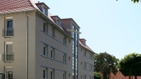 Graues Wohnhaus mit 4 Etagen, Treppenhaus große Fenster, Dach neu.