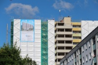 Hochhaus mit Baugerüst und weißen Planen, rechts Rohbau angebauter Aufzugsturm.