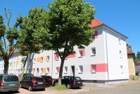 Hellgrauer Altbau mit drei Etagen, farbige Vierecke auf Fassade. Bäume und parkende Fahrzeuge. Hellgrauer Altbau mit drei Etagen, farbige Vierecke auf Fassade. Bäume und parkende Fahrzeuge.