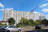140 Meter breites Hochhaus in Plattenbauweise, dahinter hoher Baukran. Bauzäune und Fahrzeuge.