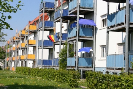 Altbauten mit sanierten Fassaden in weiß und angebauten Balkonen in gelb, blau und rot. Davor Hecken und Grünfläche. Altbauten mit sanierten Fassaden in weiß und angebauten Balkonen in gelb, blau und rot. Davor Hecken und Grünfläche.
