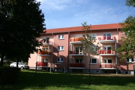 Saniertes, roséfarbenes Mehrfamilienhaus mit Satteldach und vorgestellten Balkonen, 3 Etagen. Vorne Wiese mit alten, hohen Bäumen im Sommer. Saniertes, roséfarbenes Mehrfamilienhaus mit Satteldach und vorgestellten Balkonen, 3 Etagen. Vorne Wiese mit alten, hohen Bäumen im Sommer.