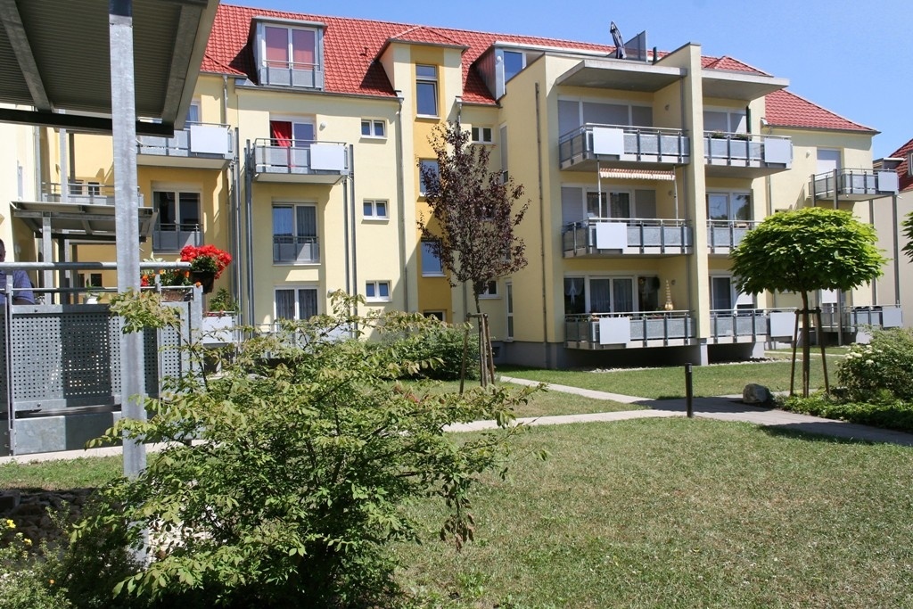 Saniertes, gelbes Wohnhaus mit Balkonen, bepflanzte Grünfläche. Saniertes, gelbes Wohnhaus mit Balkonen, bepflanzte Grünfläche.