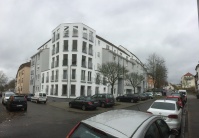 Mehrere Wohnhäuser mit 5 Etagen, Fassade weiß oder grau, vorderes Haus halbrund. Straße mit parkenden Autos. Mehrere Wohnhäuser mit 5 Etagen, Fassade weiß oder grau, vorderes Haus halbrund. Straße mit parkenden Autos.