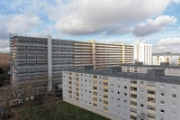 Hinten langes Hochhaus mit 15 Etagen, links Gerüst und zum Teil saniert, Mitte und rechts nicht saniert. Vorne 6geschossige Gebäude mit Flachdächern und Loggien. 