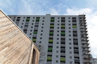 Saniertes Hochhaus, weiße Fassade, Balkonbrüstungen Grüntöne, rechts Baugerüst über 15 REtagen.