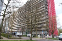 140 Meter langes Hochhaus mit 15 Etagen, links saniert, Mitte unsaniert, rechts mit Baugerüst und Netzen. Vorne Straße, Fahrzeuge, Parkplätze.