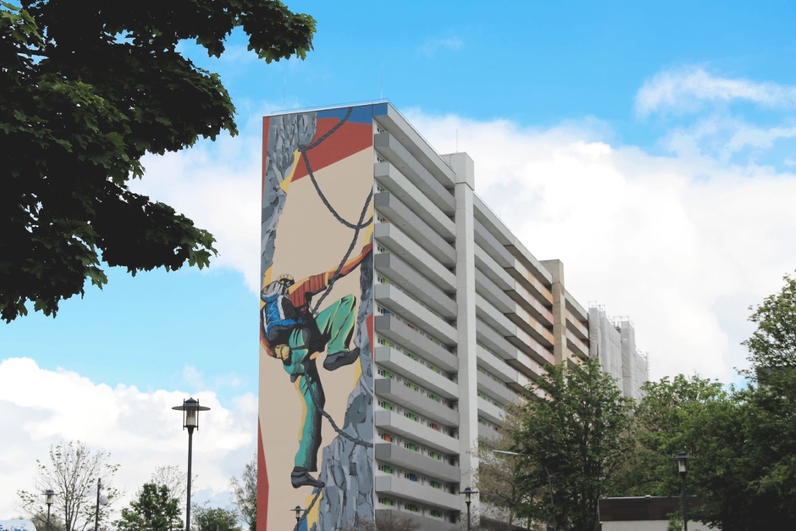 140 Meter langes Hochhaus mit 15 Etagen, saniert, vorne Laubengänge mit hellgrauen Brüstungen. Giebel mit Graffito, das einen Bergsteier zeigt. 140 Meter langes Hochhaus mit 15 Etagen, saniert, vorne Laubengänge mit hellgrauen Brüstungen. Giebel mit Graffito, das einen Bergsteier zeigt.