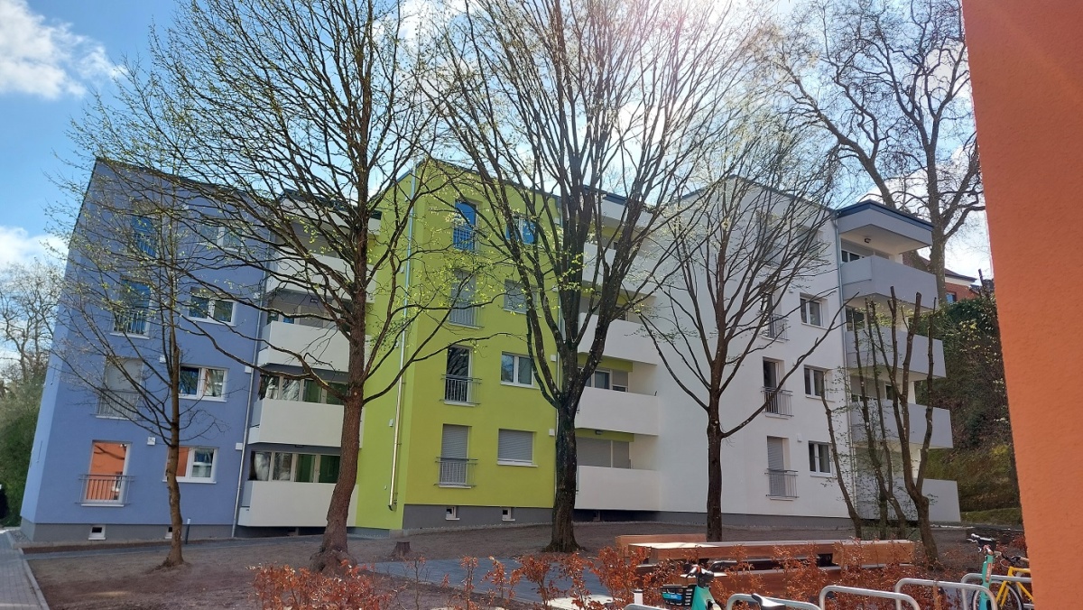 viergeschossiges Wohnhaus mit Flachdach und Balkonen, Fassade blau, grün und weiß