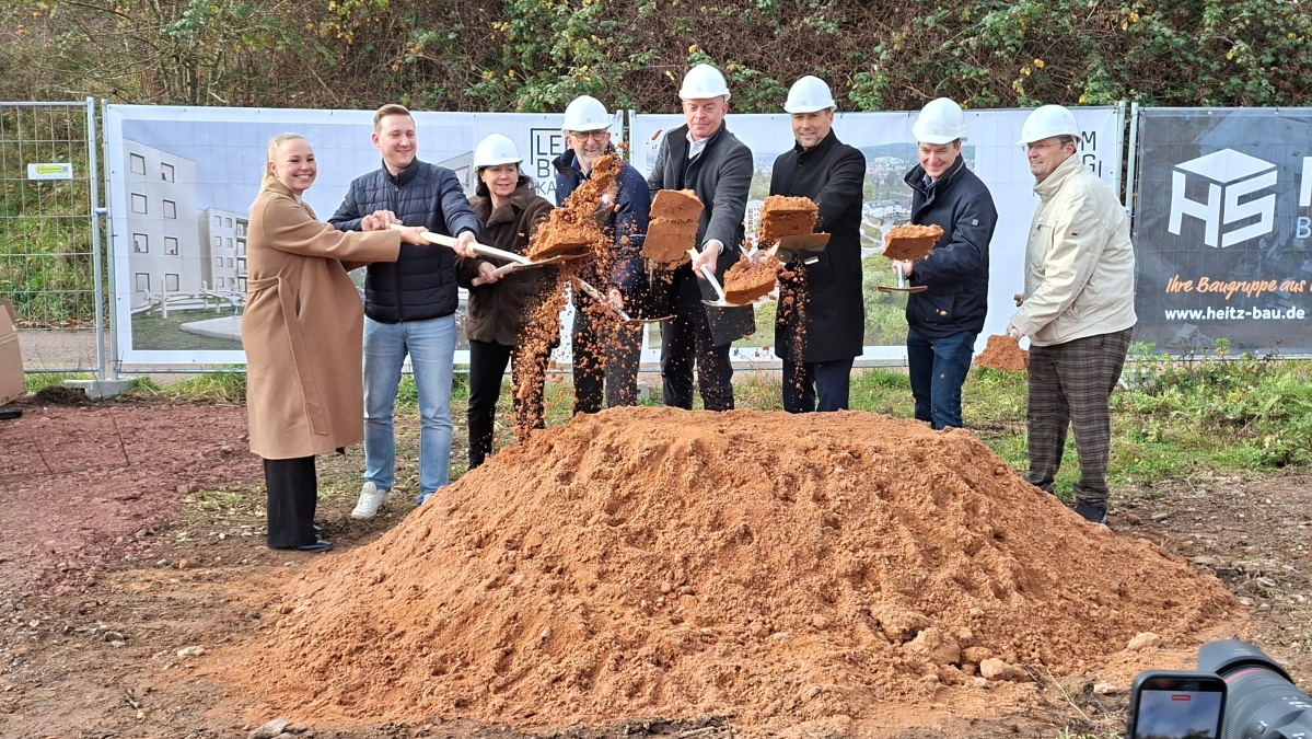 Acht Personen mit Spaten hinter einem Sandhügel.