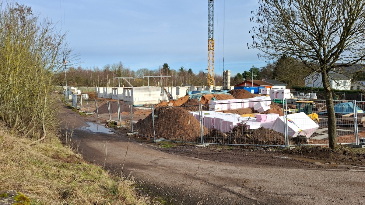 Baustelle mit Baumaterial, Bauzaun, Baukran. Im Hintergrund Erdgeschoss des 1. Rohbaus