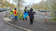 5 Personen mit Warnwesten sammeln auf Parkplatz Müll mit Greifzangen