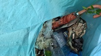 Detailaufnahme in einen Müllsack. Neben Plastikschnipseln sieht man auch einen kaputten Stockschirm