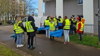 Mehrere Personen mit gelben Warnwesten, blauen Müllsäcken und Greifzangen auf einem Weg.