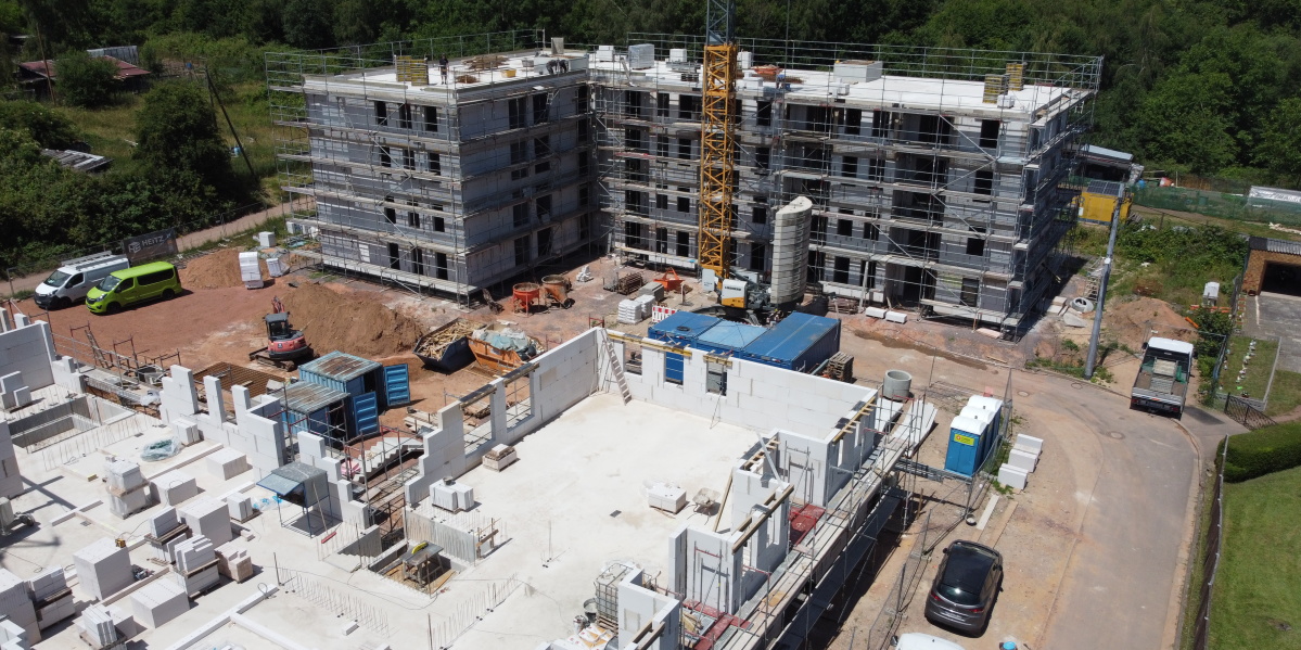 Im Vordergrund Gebäude im Bau mit einer Etage und Baugeräten auf Decke, hinten Rohbau mit 4 Etagen und Baugerüst